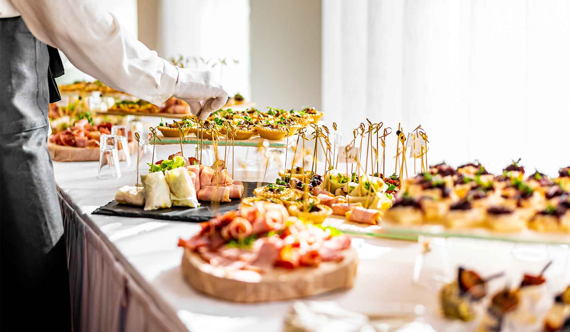 A server plating an elegant catering spread of canapés and charcuterie