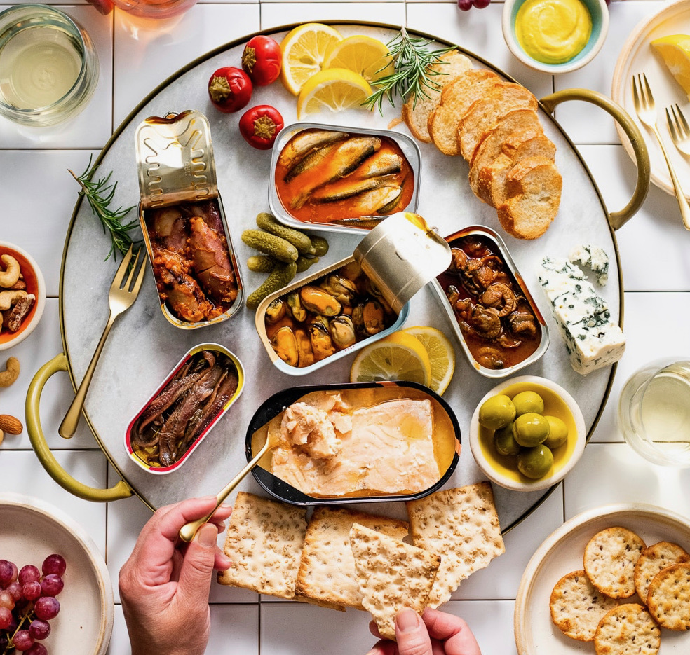 A spread of tinned fish, cheese, olives, and crackers