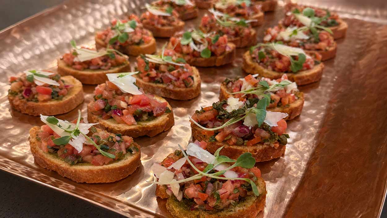 A copper tray of bruschetta with shaved parmesan and microgreens